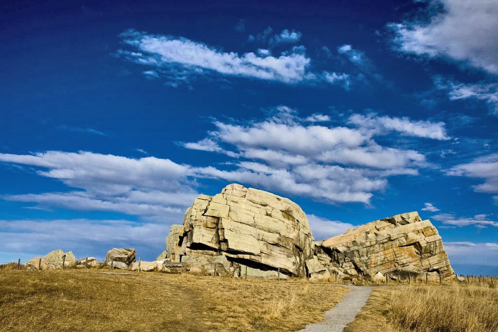A huge quartzite boulder, split into two pieces, sitting alone in a flat Alberta prairie.