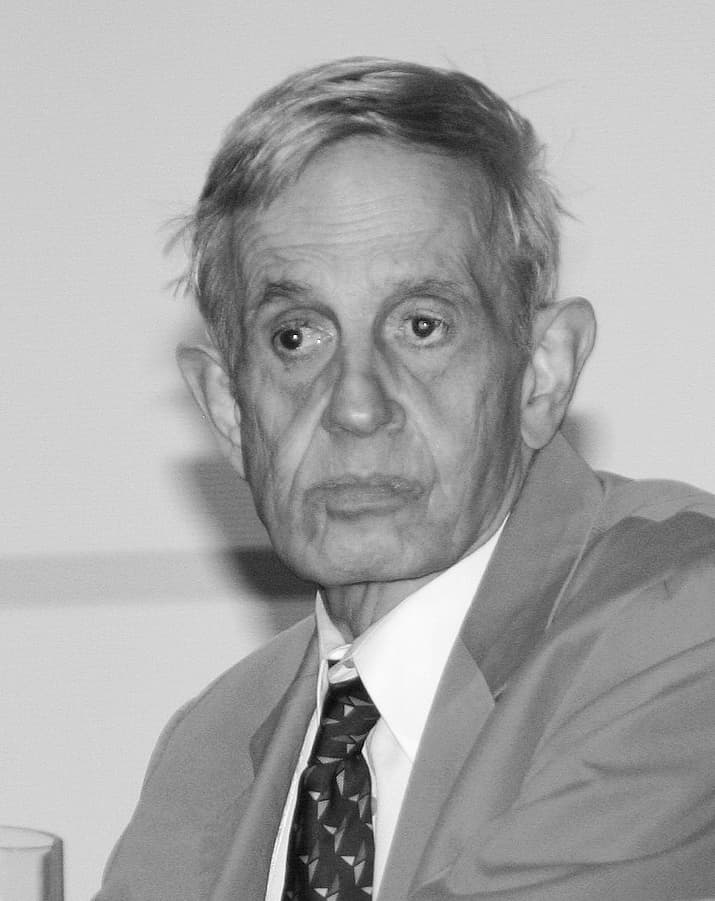 John Nash, un homme âgé aux cheveux blancs et aux lunettes, prenant la parole lors d'un symposium de théorie des jeux.