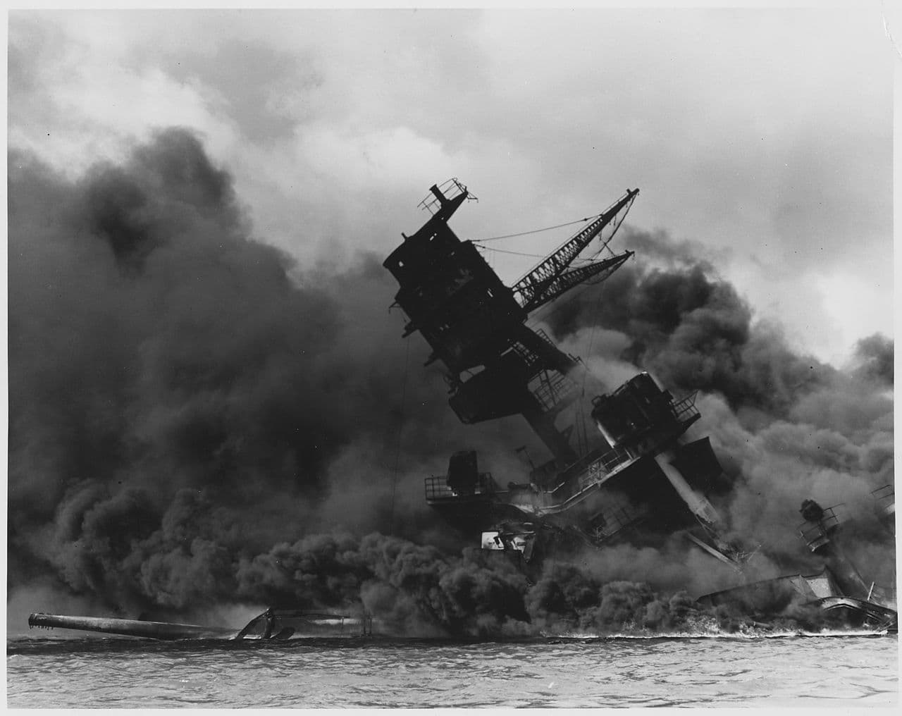 Photo en noir et blanc du cuirassé USS Arizona en feu, dégageant une épaisse fumée à Pearl Harbor après l'attaque japonaise.