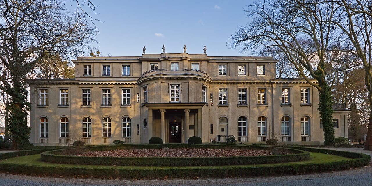 Photo d'une grande villa au bord d'un lac, murs blancs et toit de tuiles rouges, aujourd'hui un mémorial de la Shoah.