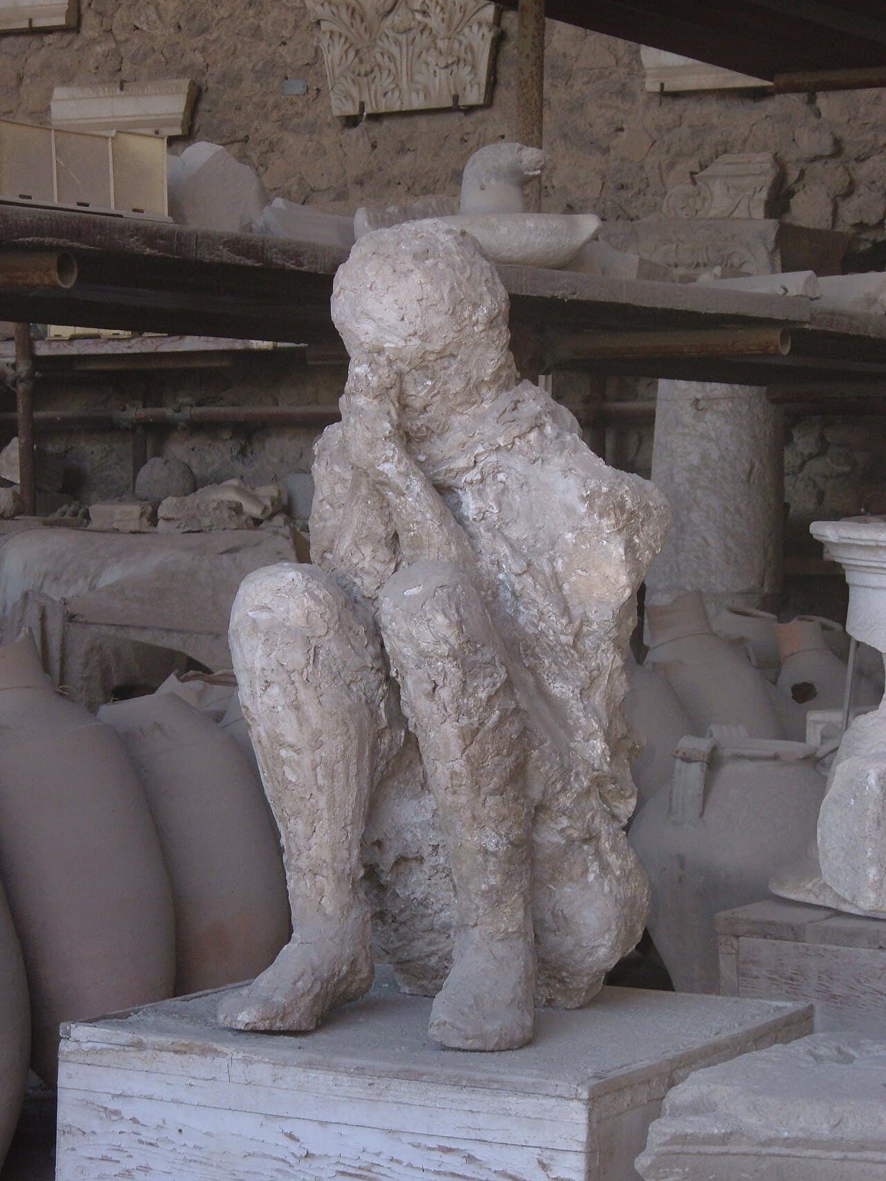 Moulage en plâtre d'une victime de Pompéi allongée recroquevillée au sol, montrant les plis des vêtements et la position du corps préservés dans la cendre.
