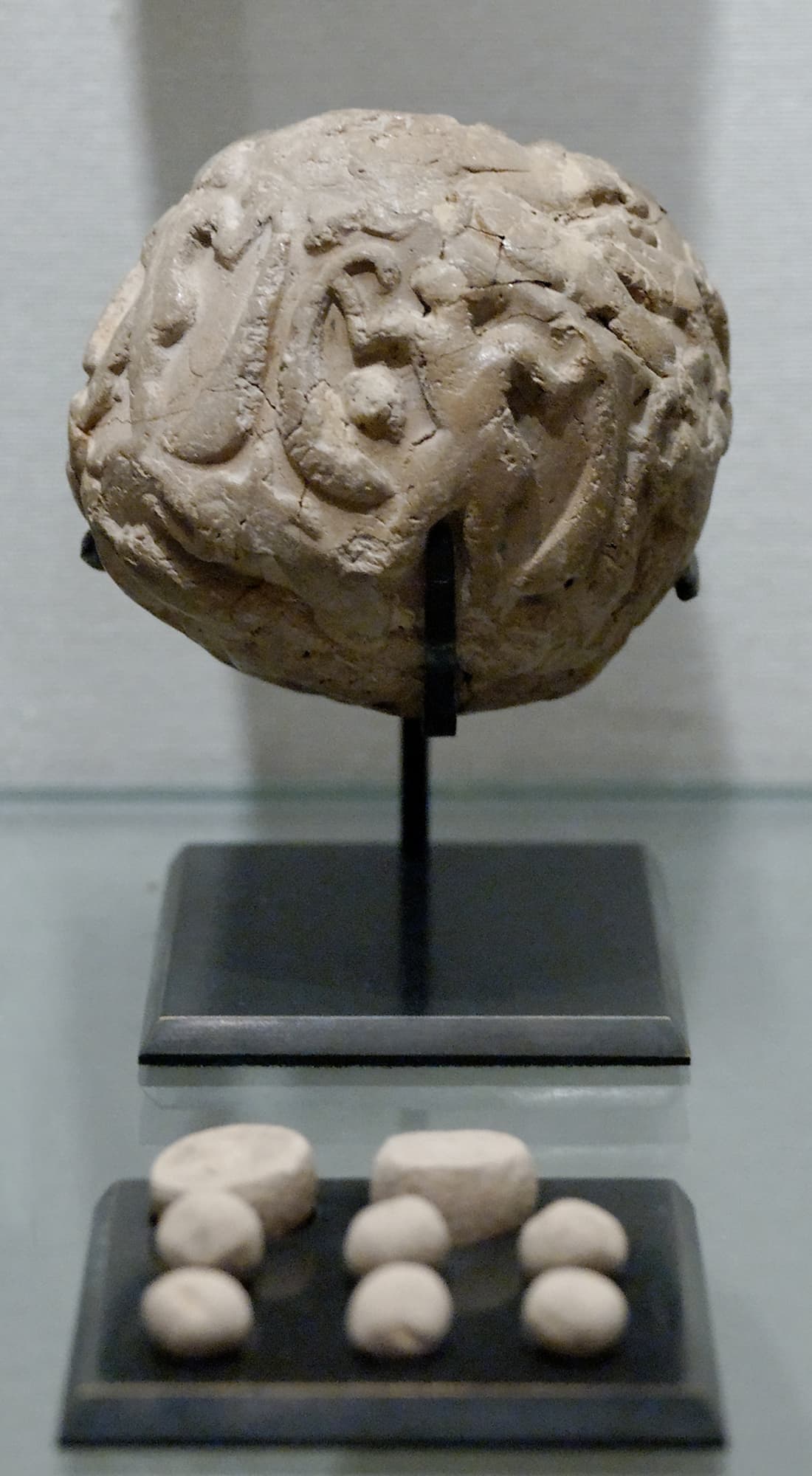Une boule d'argile rugueuse sur un support, avec huit petits jetons d'argile de formes différentes exposés en dessous.
