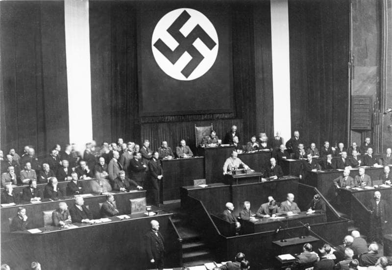 Photo en noir et blanc d'Hitler parlant à un pupitre dans l'opéra Kroll, devant des députés et un grand aigle.