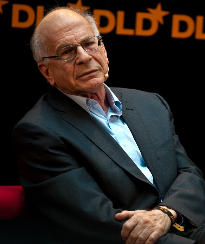 Le psychologue Daniel Kahneman, un homme âgé à lunettes et veste sombre, assis sur la scène d'une conférence.