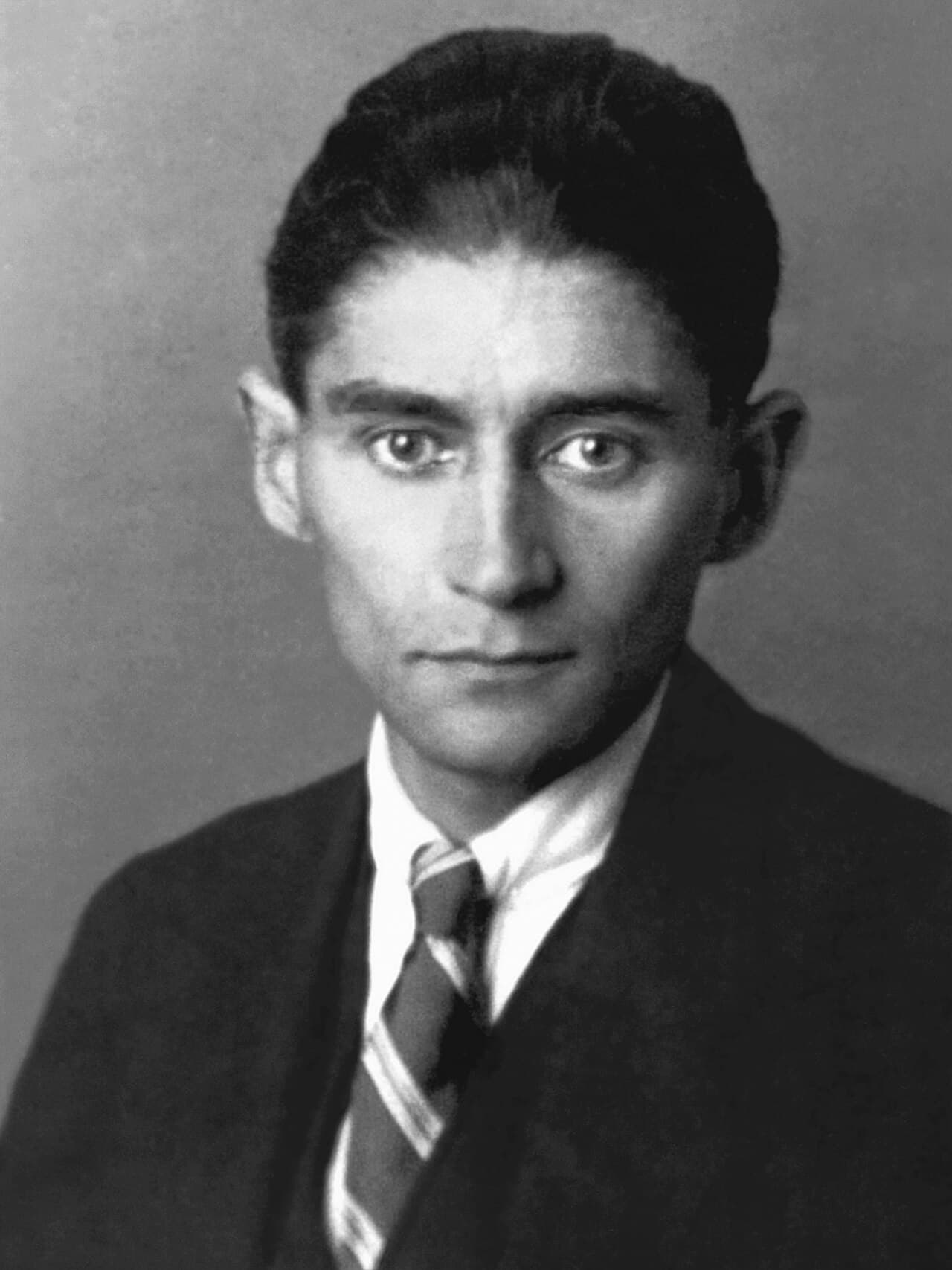 Portrait photographique en noir et blanc d'un jeune homme mince aux cheveux sombres et aux grands yeux noirs, en costume et cravate.