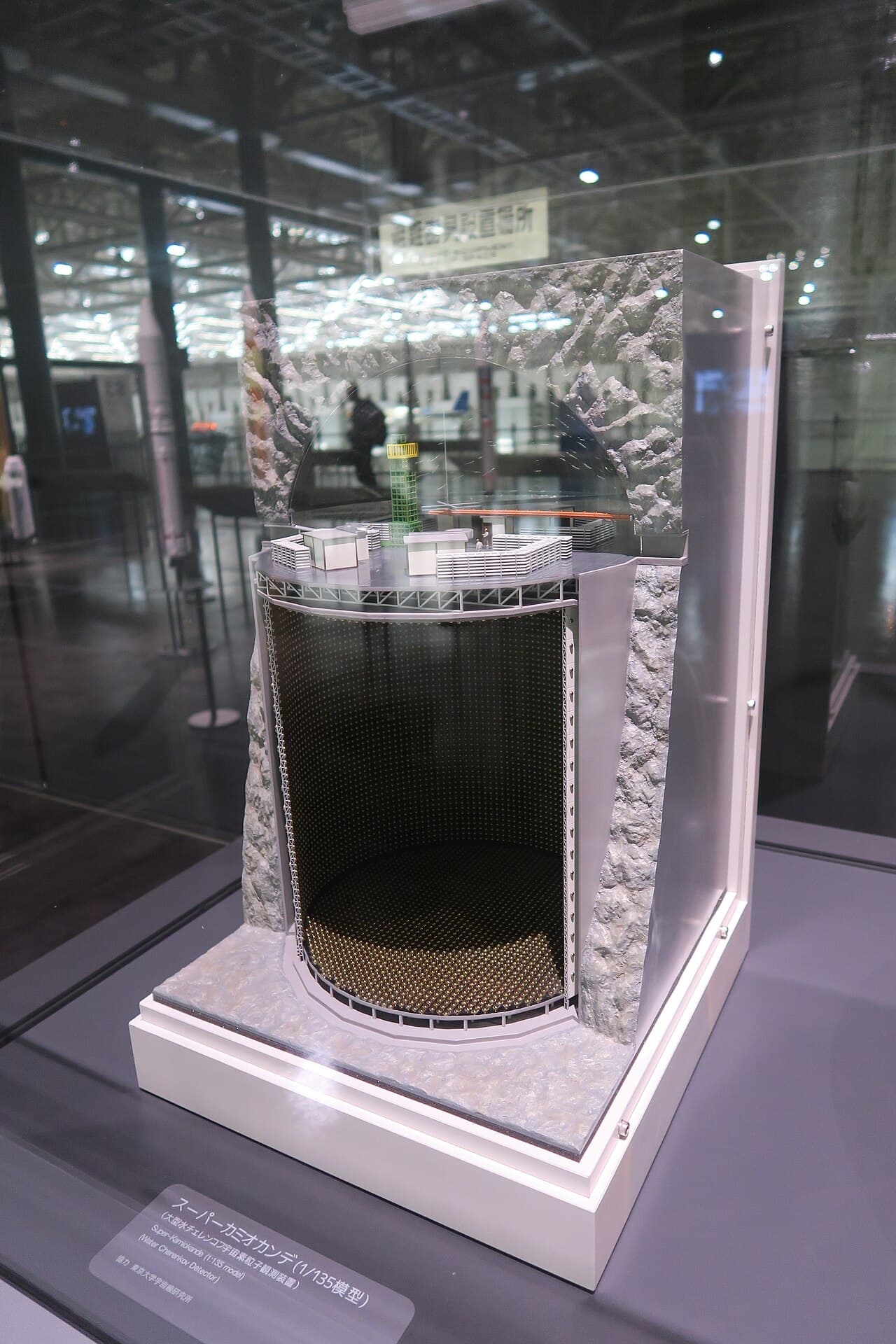 A 1-to-135 scale model of the Super-Kamiokande neutrino detector, showing a cylindrical tank lined with rows of circular sensors, displayed in a museum.