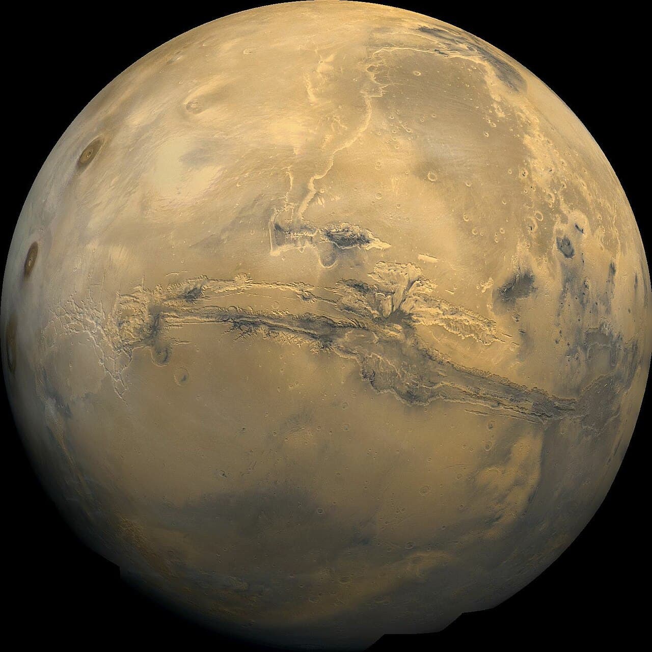 Mars vue de l'espace, un globe orange rouillé avec des taches gris foncé et le long système de canyons Valles Marineris en son milieu.