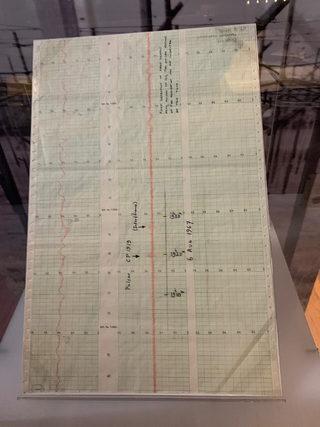 Une bande de papier d'enregistreur avec un tracé ondulé et des notes manuscrites, montrant le signal du premier pulsar.
