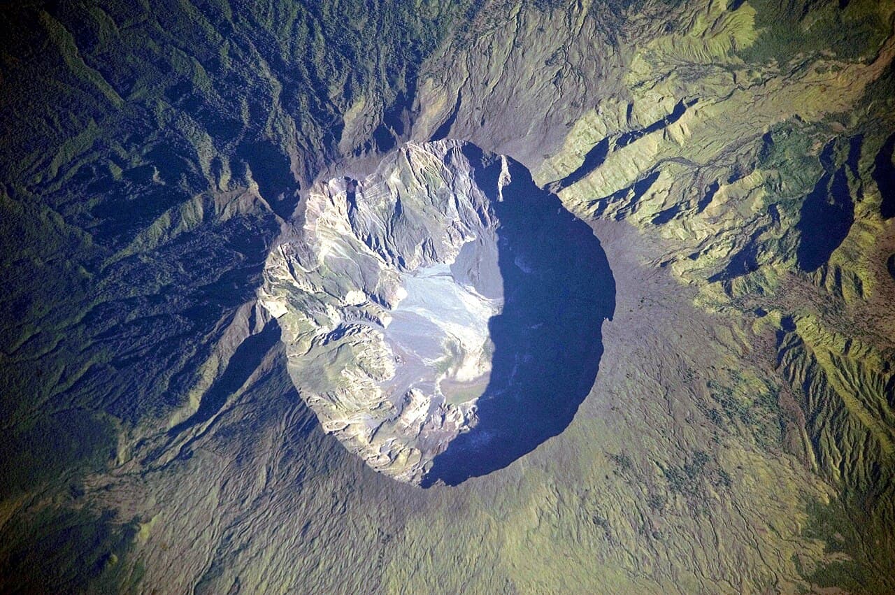 Photo prise par un astronaute : le Tambora vu d'en haut, un cratère immense et profond entouré de pentes verdoyantes.