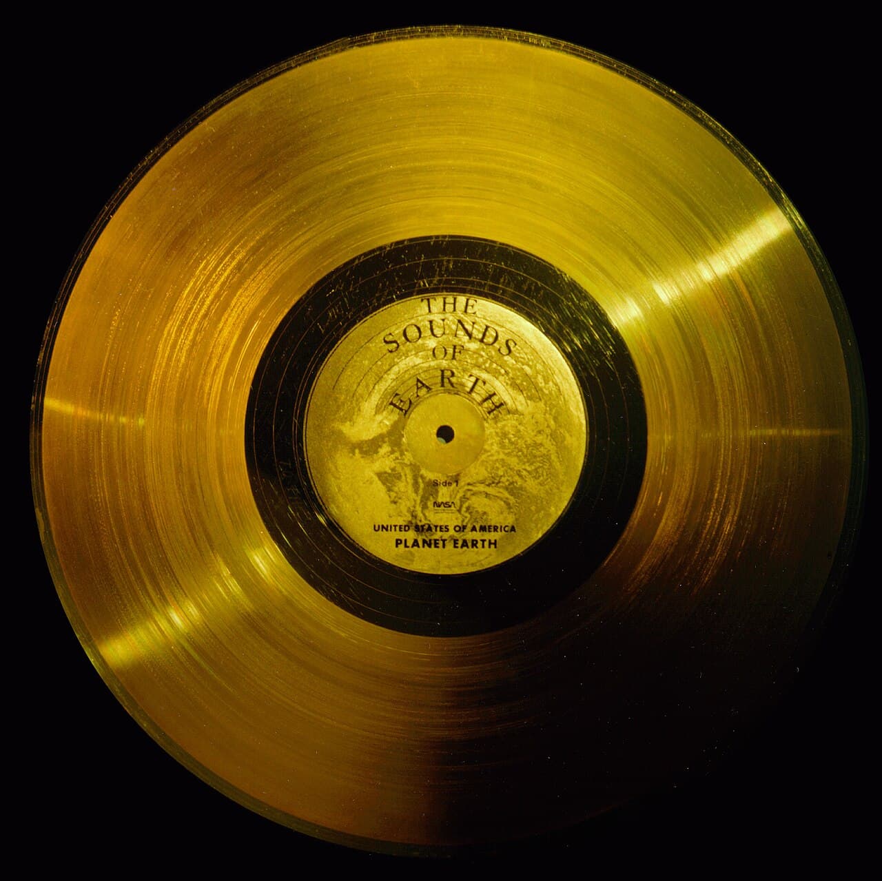 The gold-coloured Voyager record labelled 'The Sounds of Earth', lying on a dark background.