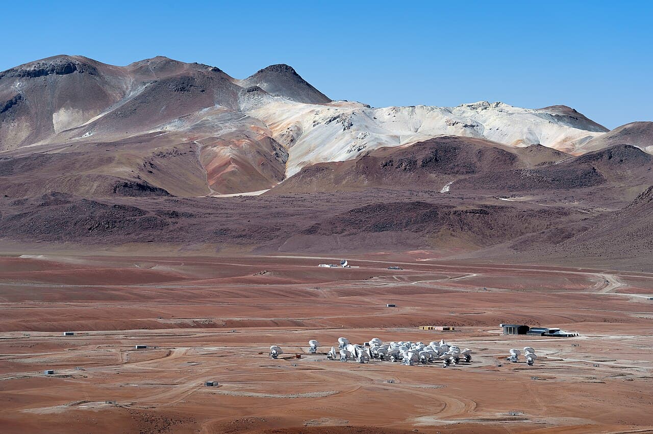 De grandes antennes paraboliques blanches du réseau ALMA dressées dans le paysage désertique et aride du désert d'Atacama.