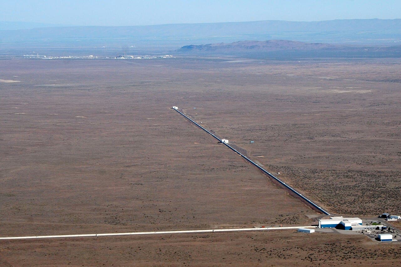 Aerial view of the LIGO Hanford Observatory in a flat desert landscape, with two long straight arms meeting at a right angle at a central building.