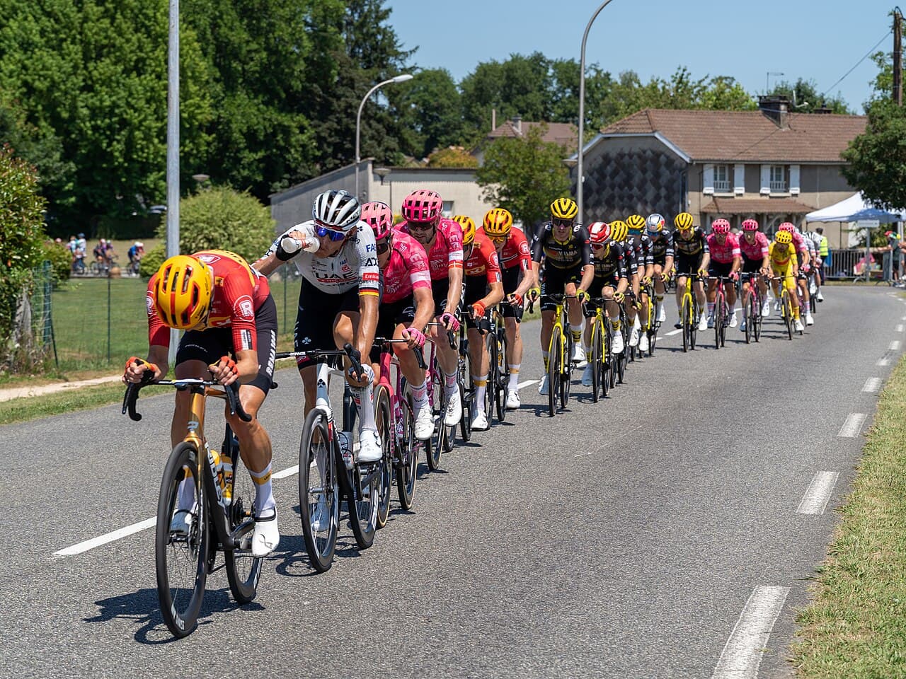 Un peloton dense de coureurs en maillots d'équipe colorés, roulant serrés sur une route du Tour de France.