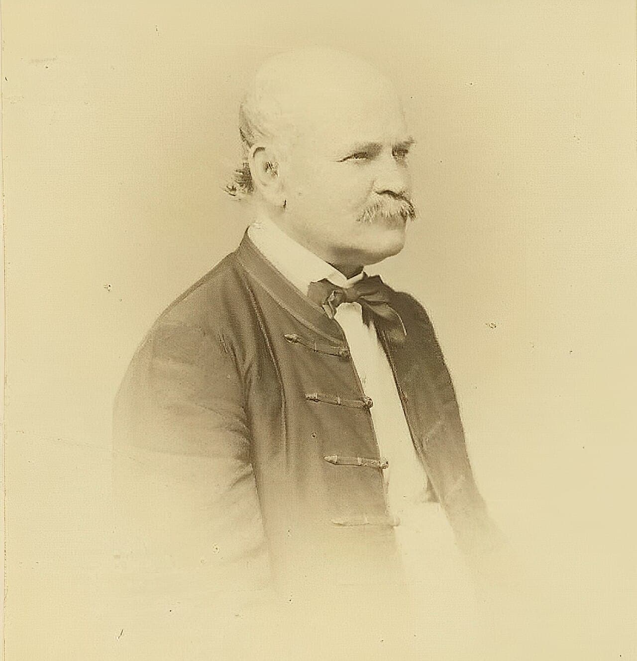 Black-and-white photograph of a balding man with sideburns and a moustache, wearing a dark jacket.